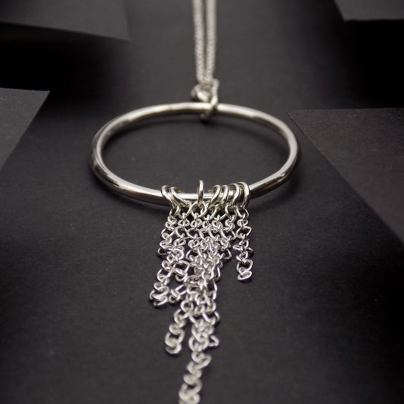 Photo vue plongeante sur un pendentif en argent formé d'un anneau auquel plusieurs chaines en argent sont soudées.