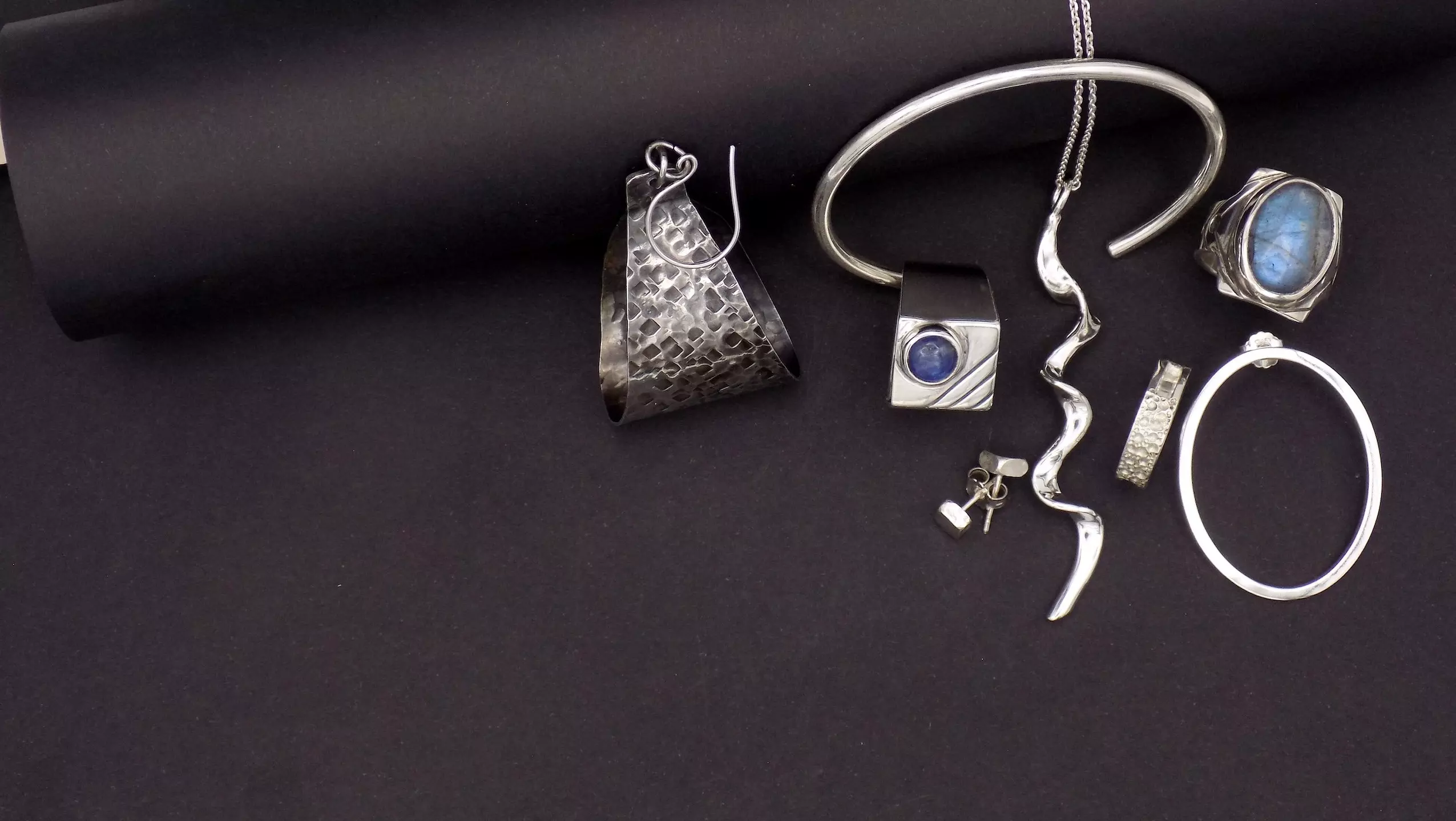 Photo de différents bijoux en argent posés sur un fond noir.