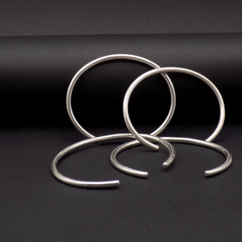 Photo sur fond noir de plusieurs bracelets ouverts en argent.