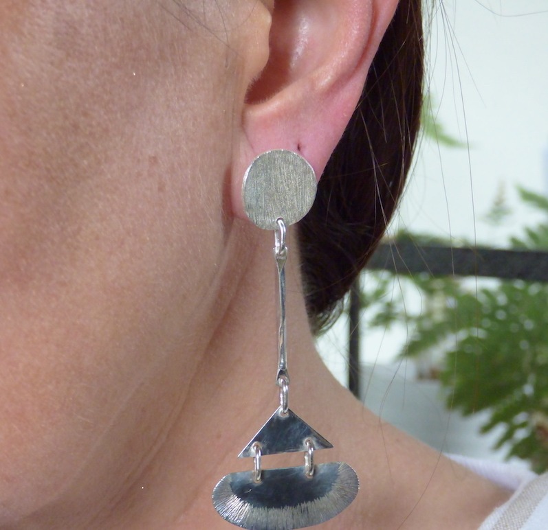 Photo couleur d'une oreille de femme portant un boucles d'oreilles longue en argent 925. La boucle est formée d'un rond puis d'un triangle sur une tige. Style art déco