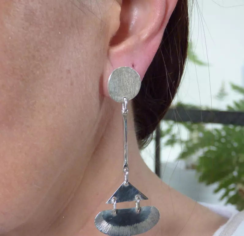 Photo couleur d'une oreille de femme portant un boucles d'oreilles longue en argent 925. La boucle est formée d'un rond puis d'un triangle sur une tige. Style art déco