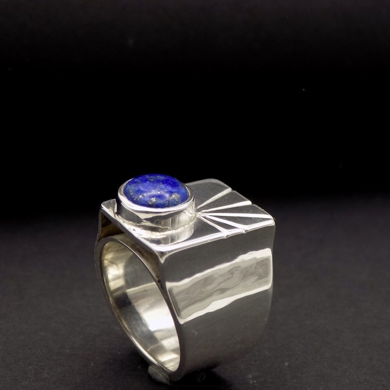 Photo couleur d'une bague chevalière de profile. Sur le dessus, il y a une pierre ronde de Lapis Lazuli et des stries qui font comme un soleil