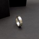 Photo sur fond noir d'une bague posée sur sa tranche. C'est une bague en argent pour homme.