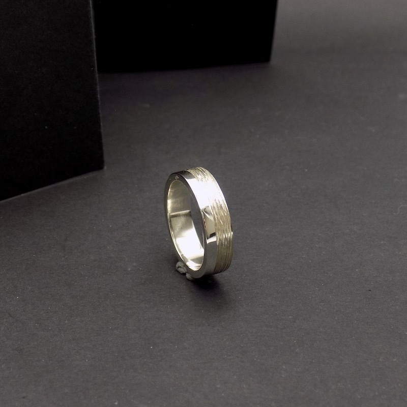Photo sur fond noir d'une bague posée sur sa tranche. C'est une bague en argent pour homme.