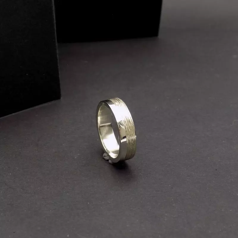 Photo sur fond noir d'une bague posée sur sa tranche. C'est une bague en argent pour homme.