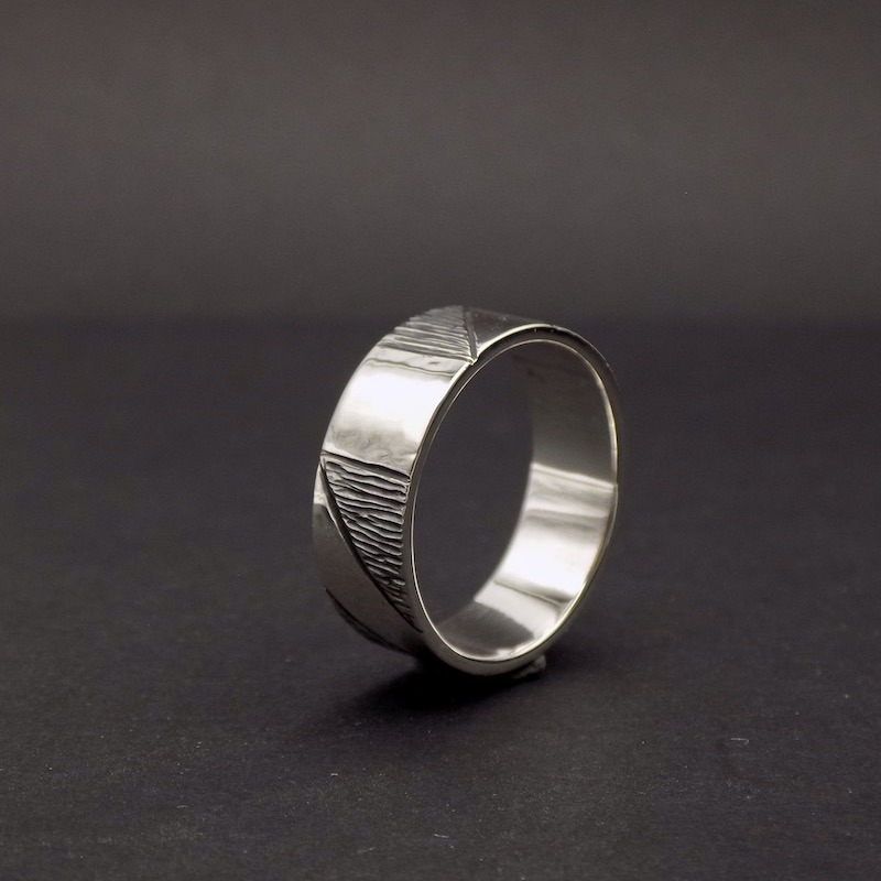 Photo sur fond sombre d'une bague large pour homme en argent posée sur sa tranche.