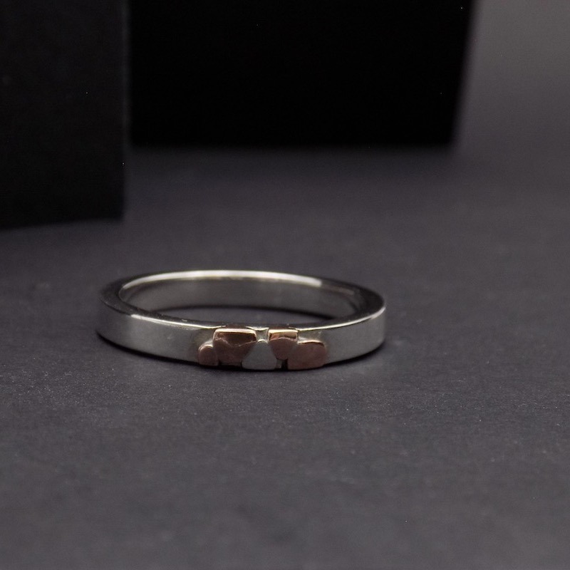 Photo d'une bague en argent posée sur un fond noir. Cette bague est fine mais épaisse. Cuivre et argent