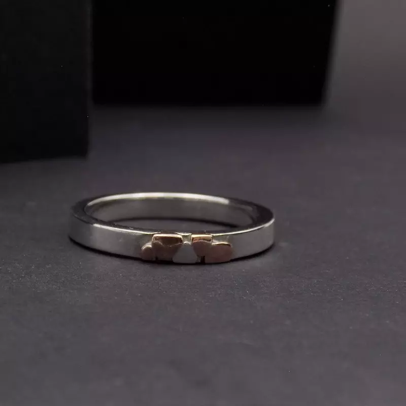 Photo d'une bague en argent posée sur un fond noir. Cette bague est fine mais épaisse. Cuivre et argent