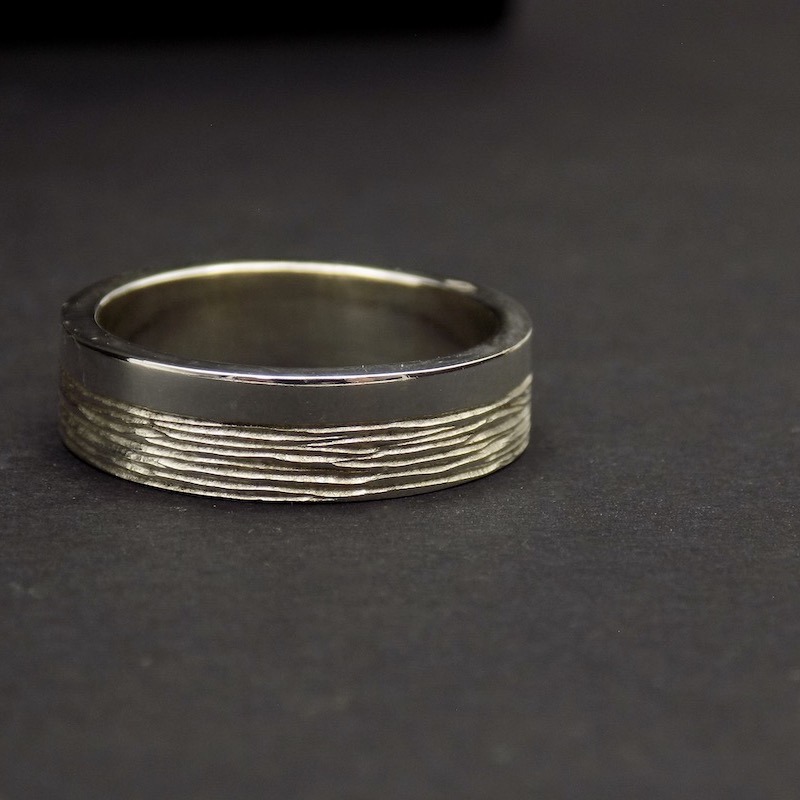 Photo en gros plan d'une bague large en argent massif pour homme. La photo est prise sur un fond noir.