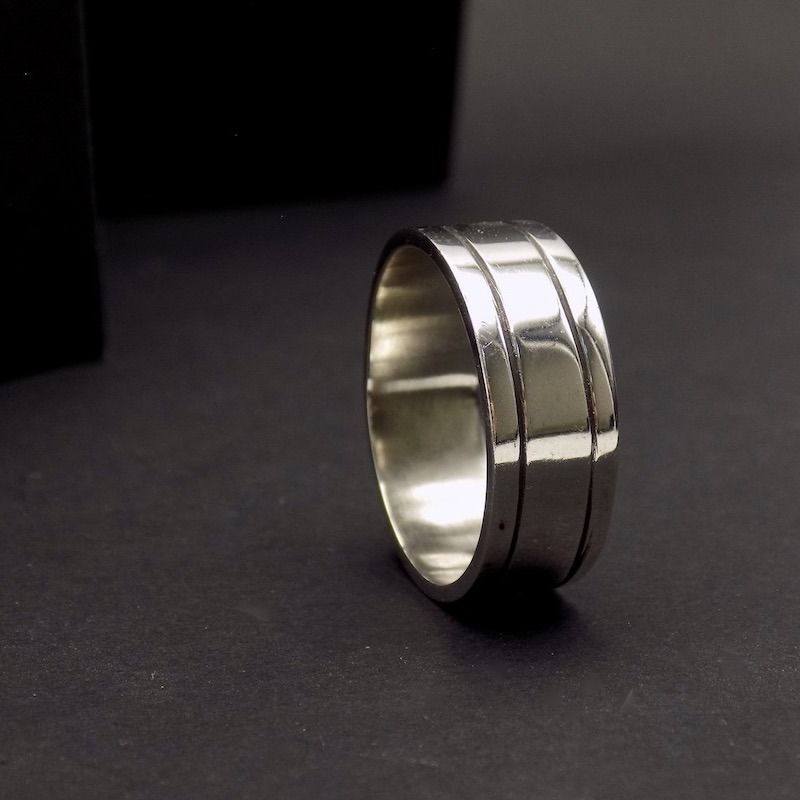 Photo sur fond noir d'une bague en argent925 large. Elle est pour homme. Elle comporte deux sillons de chaque coté