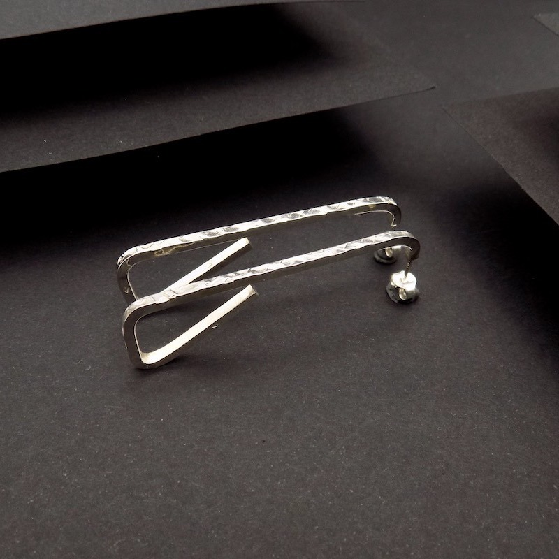 Photo couleur d'une paire de boucles d'oreilles faites en argent 925 à partir d'un fil carré. Elles sont posées sur un fond noir ce qui les fait ressortir.