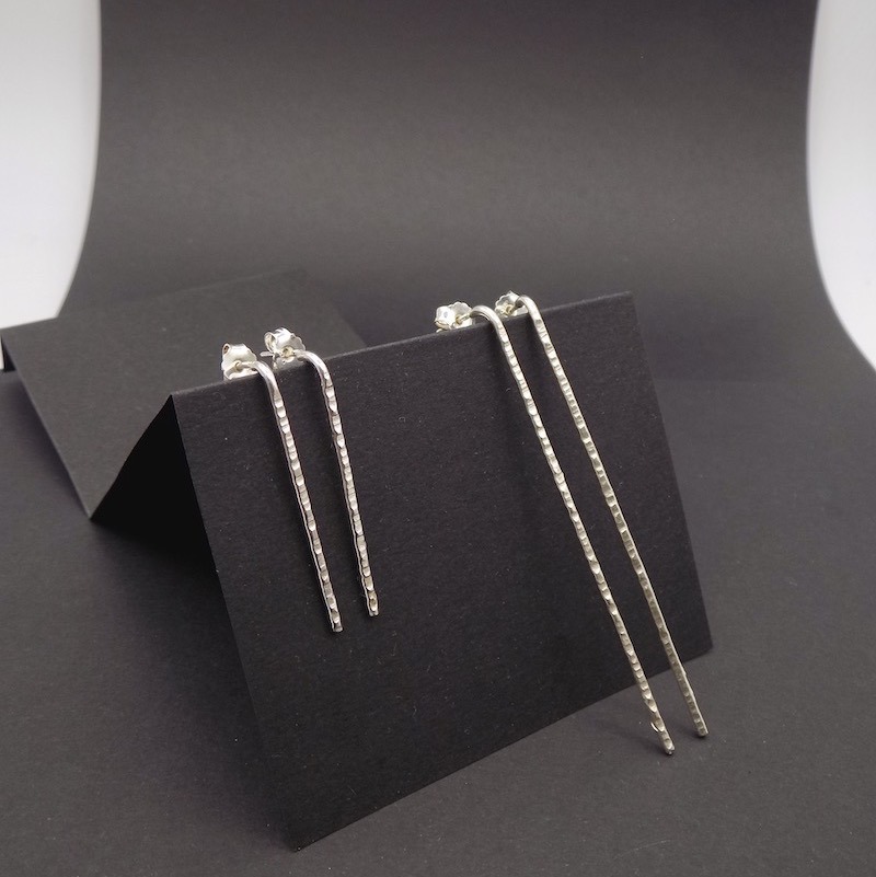 Photo de deux paires de boucles d'oreilles en argent925 longilignes et martelées qui sont posées sur un support noir.