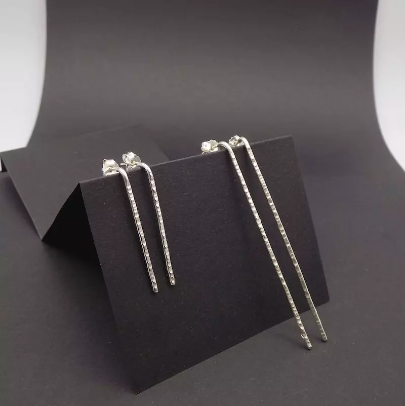 Photo de deux paires de boucles d'oreilles en argent925 longilignes et martelées qui sont posées sur un support noir.