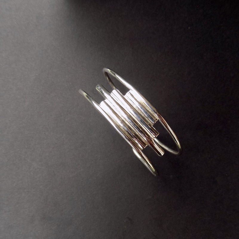 Photo d'une vue de dessus d'un bracelet manchette en argent sur fond noir.