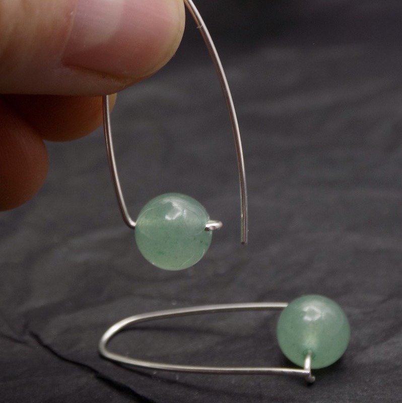 Photo gros plan d'une paire de boucles d'oreilles dont une est prise par deux doigts.