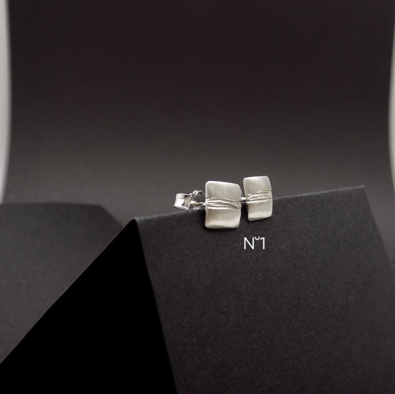 Photo de boucles d'oreilles puces en forme carrée en argent 925 posées sur un carton noir.