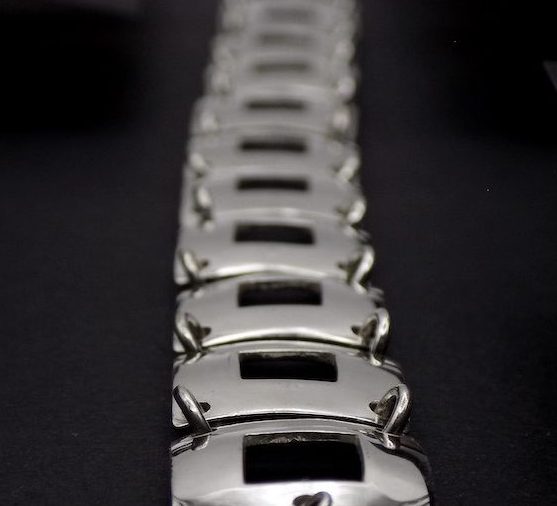 Photo foncée d'un bracelet en argent. La photo est une vue plongeante sur la longueur du bracelet. On voit bien le premier plan tandis que le second plan est flou.